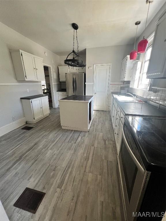 kitchen featuring a center island, stainless steel appliances, white cabinetry, a sink, and wood finished floors