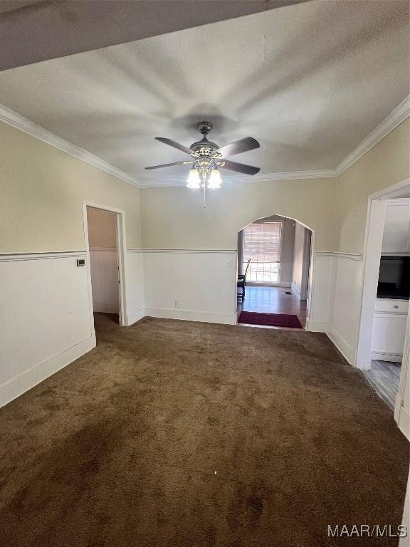 spare room featuring ornamental molding, carpet, arched walkways, and a ceiling fan