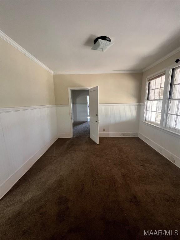 spare room featuring ornamental molding, dark colored carpet, and wainscoting