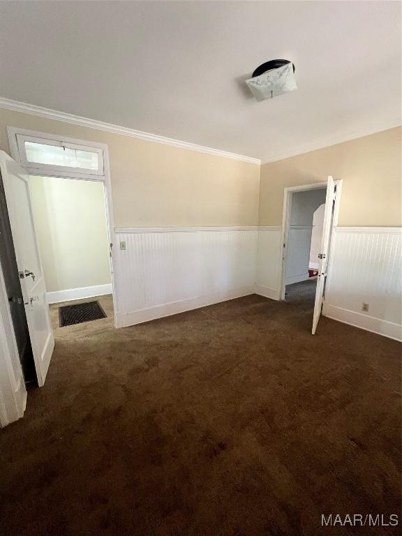 unfurnished room with ornamental molding, dark colored carpet, a wainscoted wall, and visible vents