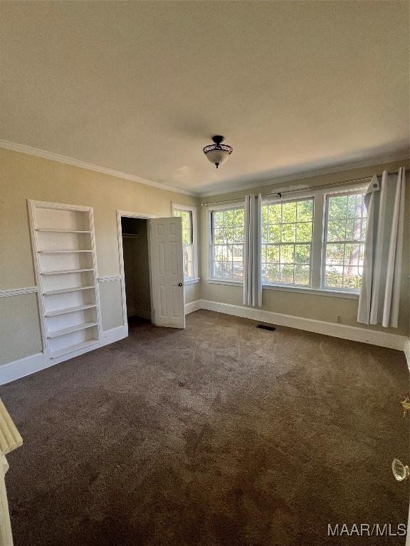 unfurnished bedroom featuring baseboards, visible vents, dark colored carpet, and crown molding