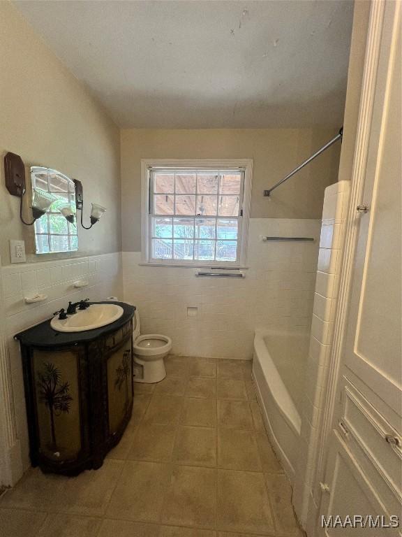 full bath with tile walls, toilet, wainscoting, vanity, and tile patterned floors