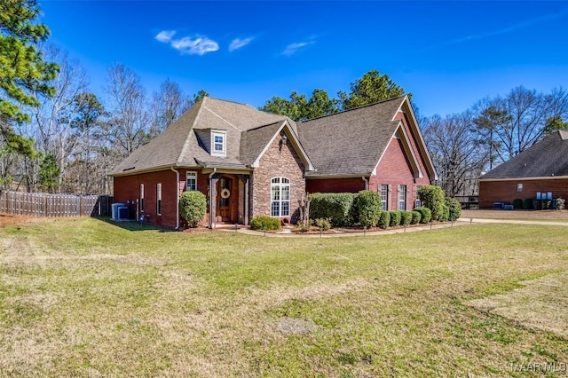 view of front of property with a front lawn, fence, brick siding, and a shingled roof