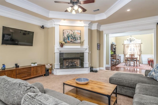 living area featuring visible vents, crown molding, a tiled fireplace, light carpet, and ceiling fan with notable chandelier