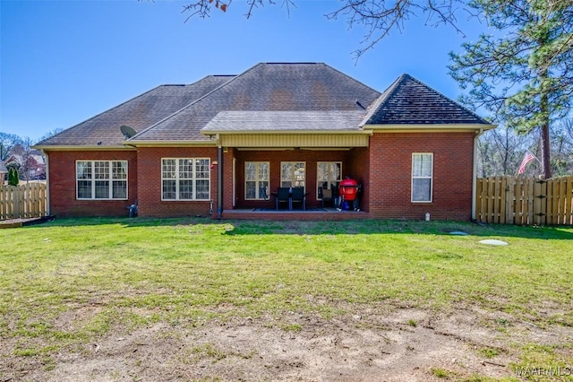 back of property with brick siding, a lawn, a ceiling fan, and fence