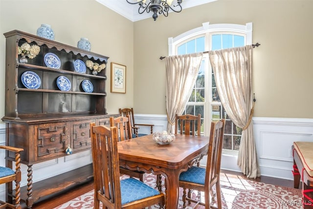 dining area with a wainscoted wall, an inviting chandelier, wood finished floors, and crown molding