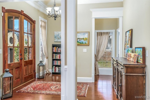 entryway featuring dark wood finished floors, a chandelier, crown molding, and baseboards