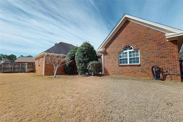 view of property exterior with brick siding, a lawn, and fence