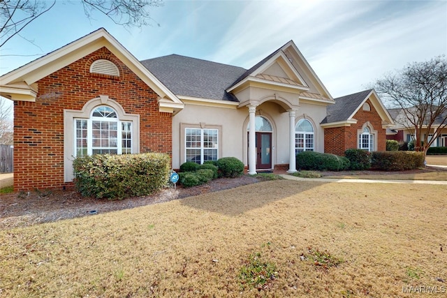 view of front facade featuring a front yard, brick siding, roof with shingles, and stucco siding