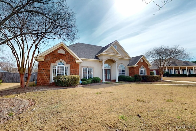 view of front of property featuring a front yard, fence, brick siding, and stucco siding