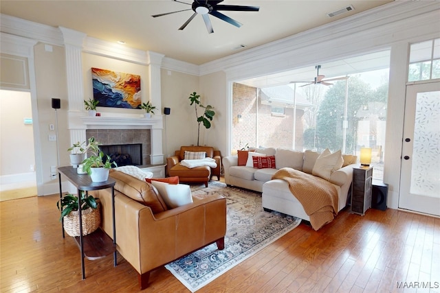 living room featuring visible vents, a tiled fireplace, ornamental molding, hardwood / wood-style floors, and a ceiling fan