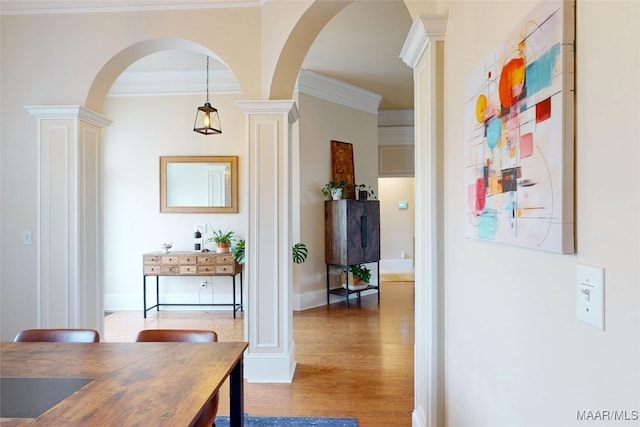 hall featuring wood finished floors, baseboards, ornate columns, arched walkways, and ornamental molding