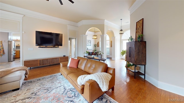 living area featuring ornamental molding, arched walkways, light wood finished floors, decorative columns, and baseboards