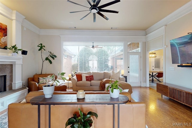 living area with visible vents, ornamental molding, a fireplace, wood finished floors, and a ceiling fan