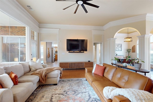 living room featuring light wood finished floors, crown molding, ceiling fan, arched walkways, and ornate columns