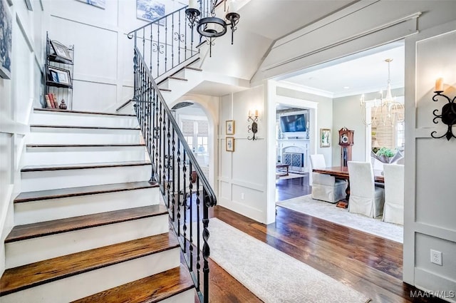 stairway featuring wood finished floors, arched walkways, crown molding, a decorative wall, and a notable chandelier