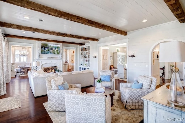 living room featuring visible vents, beam ceiling, a warm lit fireplace, wood finished floors, and arched walkways