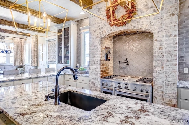 kitchen featuring light stone counters, range with two ovens, a sink, decorative backsplash, and glass insert cabinets