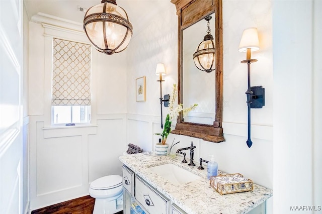 bathroom with a wainscoted wall, toilet, wood finished floors, a decorative wall, and vanity