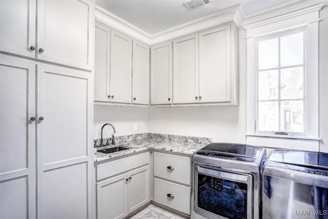 kitchen featuring visible vents, light stone countertops, washer and clothes dryer, white cabinetry, and a sink