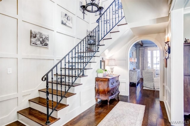 foyer with stairway, arched walkways, wood finished floors, and a decorative wall