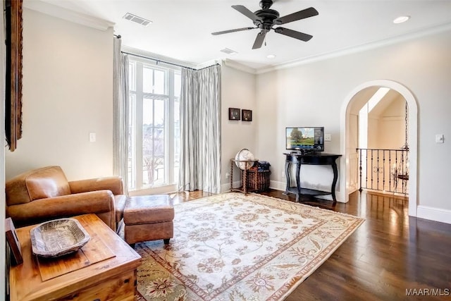 living area with dark wood-style floors, visible vents, arched walkways, and ornamental molding