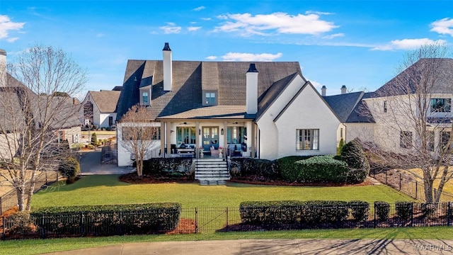 rear view of property with a porch, a yard, stucco siding, a chimney, and a fenced front yard