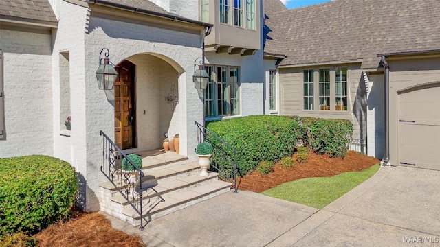 entrance to property featuring a garage and a shingled roof