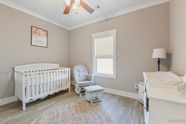 bedroom featuring wood finished floors, baseboards, visible vents, ornamental molding, and a nursery area