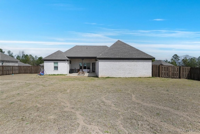 rear view of property featuring a patio, roof with shingles, a yard, a fenced backyard, and brick siding