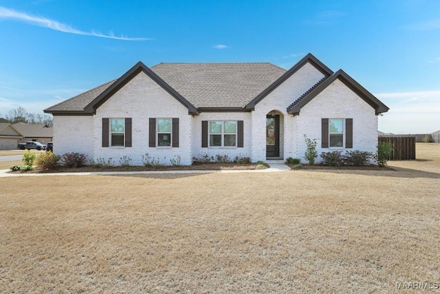 french provincial home with brick siding, roof with shingles, and a front lawn