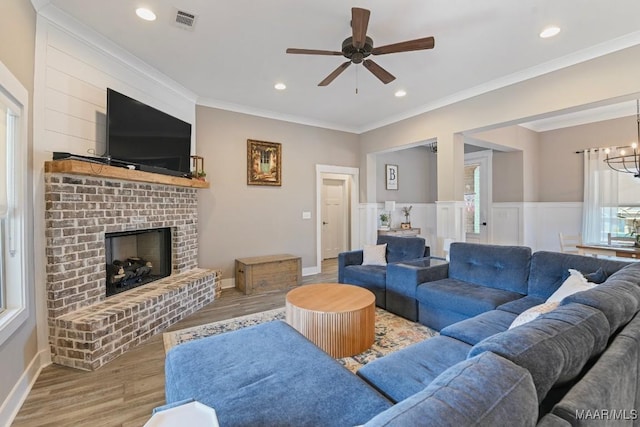 living area with wood finished floors, visible vents, recessed lighting, crown molding, and a brick fireplace