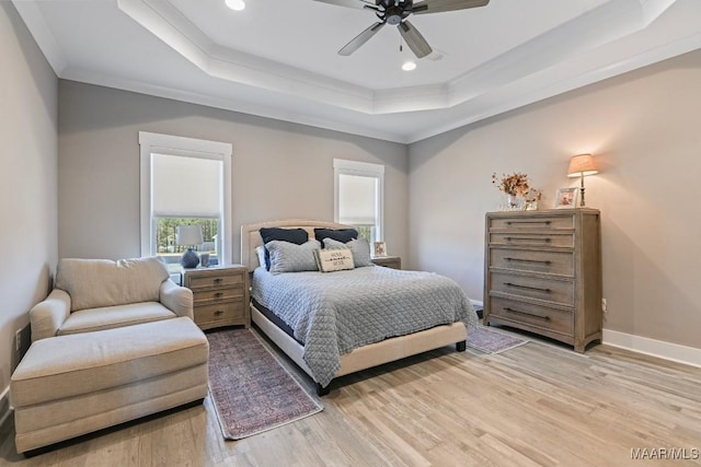 bedroom featuring a raised ceiling, crown molding, baseboards, and light wood finished floors