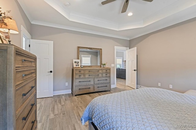 bedroom with a tray ceiling, light wood-style flooring, multiple windows, and baseboards