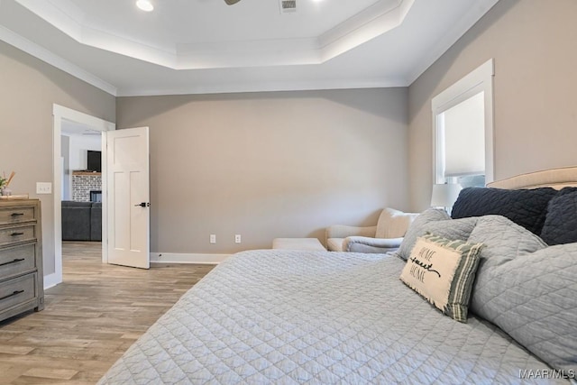 bedroom with a raised ceiling, light wood-style floors, baseboards, and ornamental molding