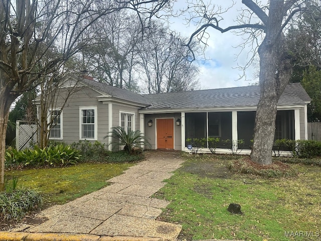 ranch-style house with a shingled roof, a front yard, and a sunroom