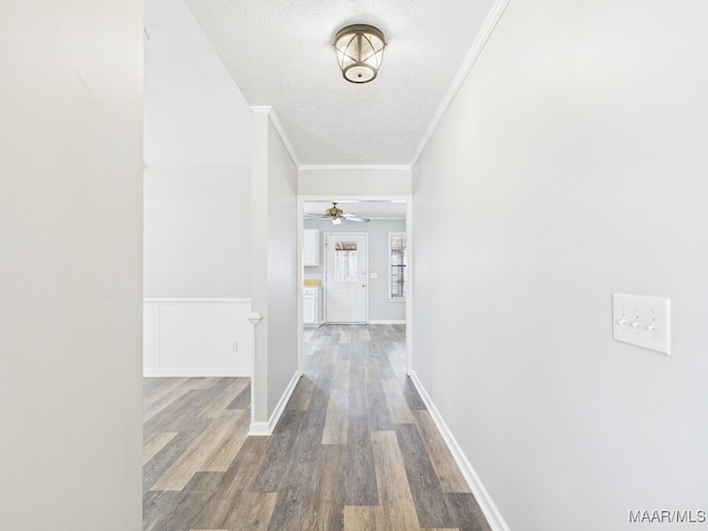 corridor with crown molding, wood finished floors, baseboards, and a textured ceiling