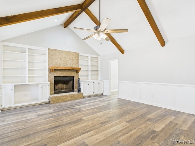 unfurnished living room featuring a ceiling fan, wood finished floors, a wainscoted wall, vaulted ceiling with beams, and a fireplace