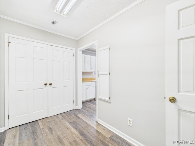 unfurnished bedroom featuring visible vents, baseboards, light wood-type flooring, ornamental molding, and a closet