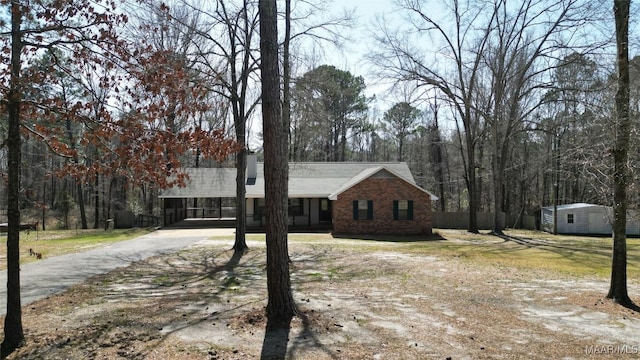 view of front of house with an outbuilding, driveway, a storage shed, a carport, and brick siding