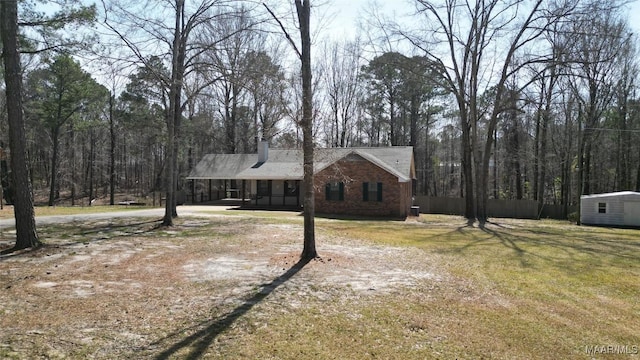 view of front facade featuring brick siding, a front lawn, fence, a chimney, and an outbuilding