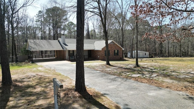 view of front of property featuring a chimney, driveway, an outdoor structure, an attached carport, and brick siding