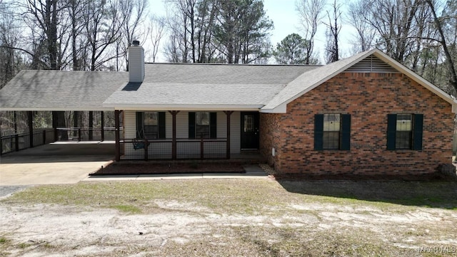 ranch-style home featuring brick siding, a shingled roof, a porch, a chimney, and driveway