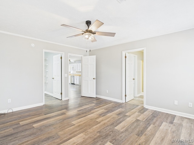 interior space with ornamental molding, a ceiling fan, baseboards, and wood finished floors