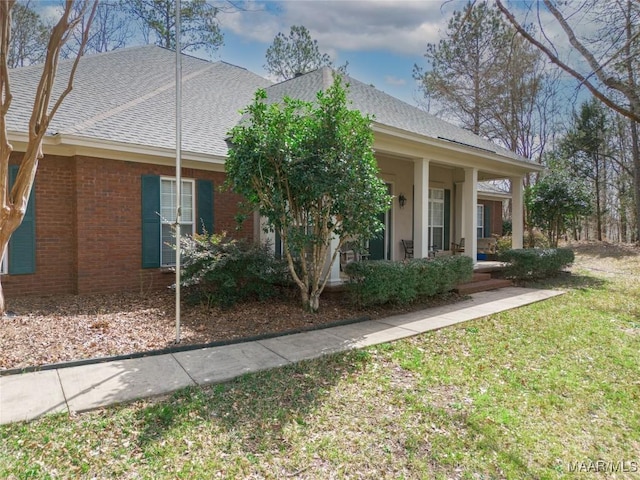 view of front facade featuring brick siding, a porch, a front yard, and a shingled roof