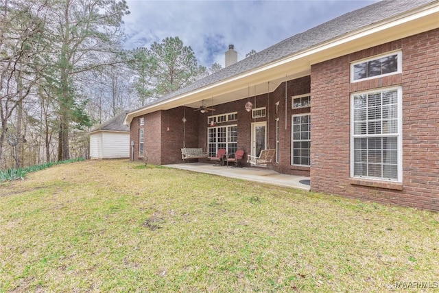 back of house with a yard, brick siding, ceiling fan, a chimney, and a patio area