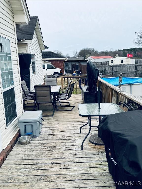 wooden terrace with outdoor dining area, fence, and a fenced in pool