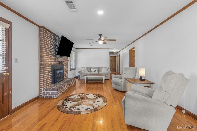 living room with visible vents, a brick fireplace, crown molding, ceiling fan, and wood finished floors