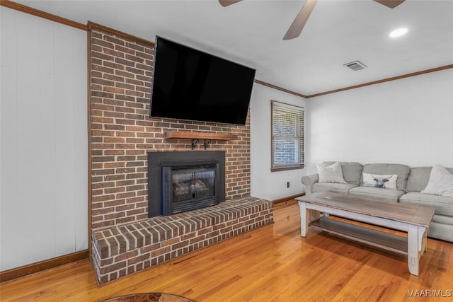 living area with hardwood / wood-style floors, a brick fireplace, visible vents, and ornamental molding