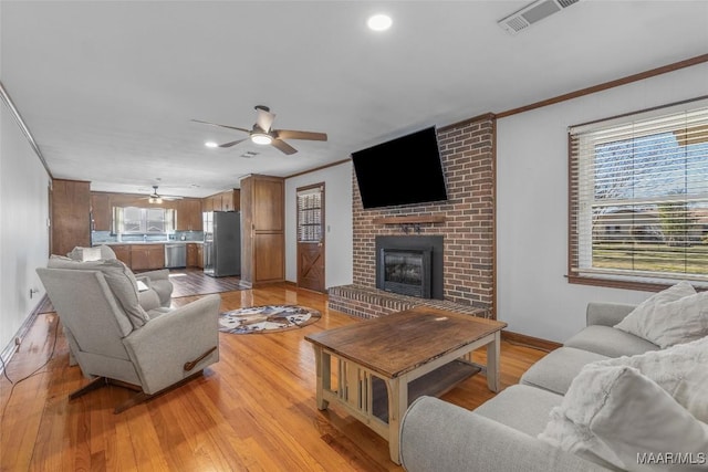 living area featuring light wood-type flooring, visible vents, ornamental molding, a ceiling fan, and a fireplace